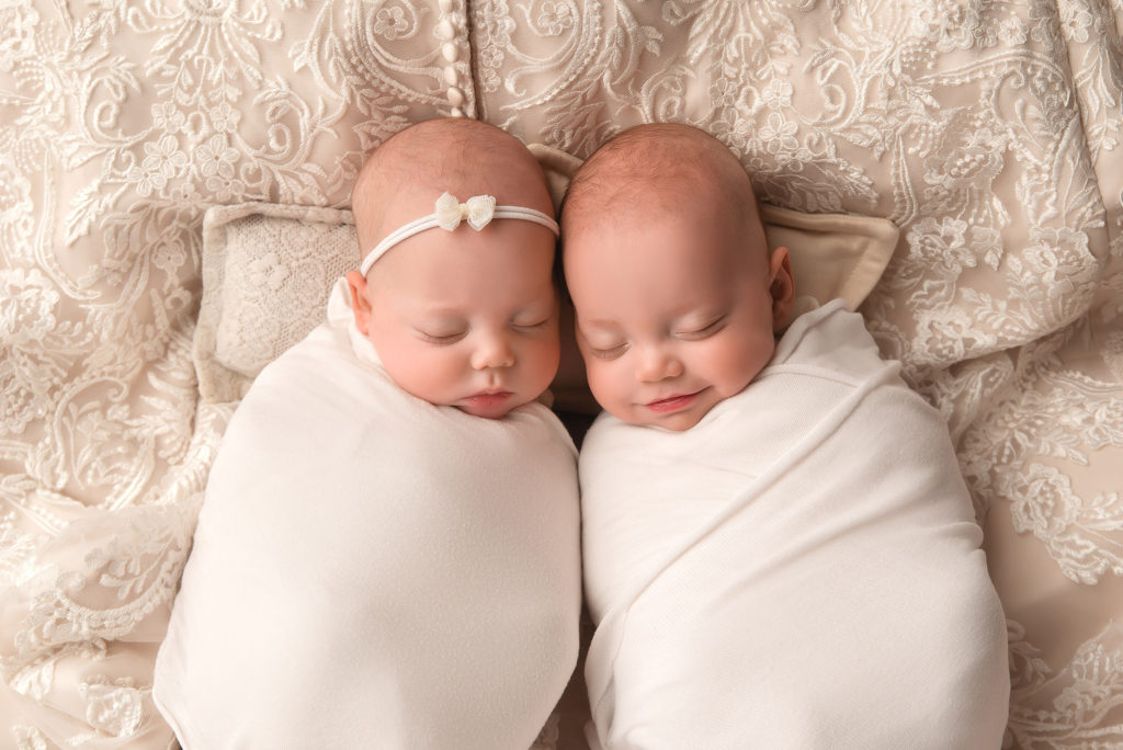 twins lay swaddled up on mother's wedding gown
